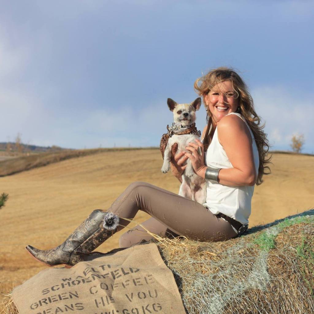 Kyla sitting in the country surrounded by yellow grass, holding an adopted dog